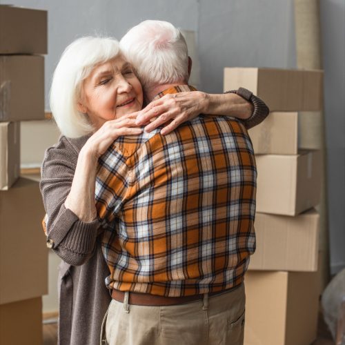 senior woman with closed eyes hugging husband in new house, moving concept